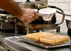 Chef Hicham bestrooit de Brusselse wafels met poedersuikerfoto © LekkerAntwerpen.be 2024 